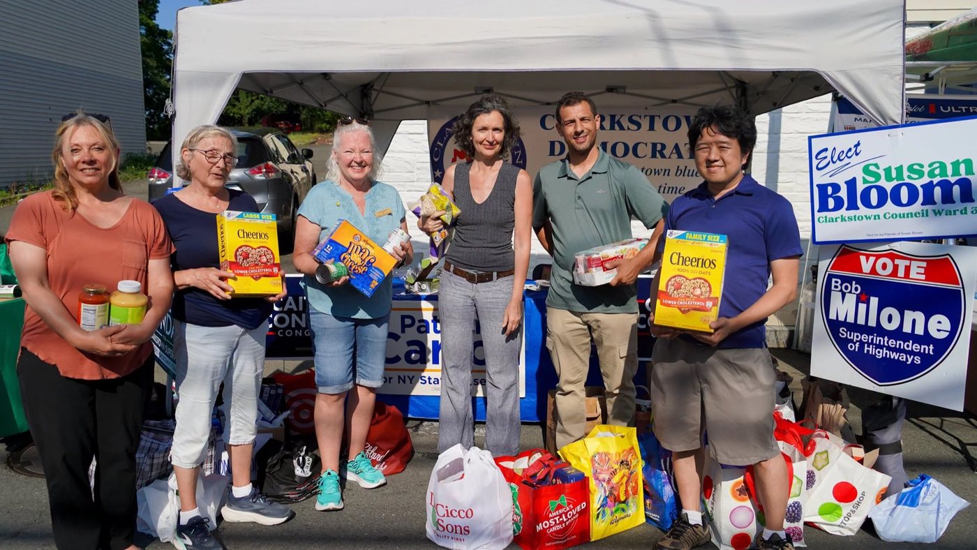 Susan Bloom and Clarkstown Democrats volunteers at a food drive under the party tent, with a Susan Bloom lawn sign beside them